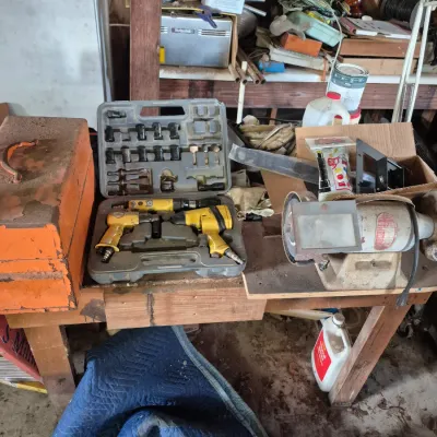 Sale Photo Thumbnail #106: Collection of workshop tools on a wooden workbench, featuring a pneumatic air tool set in a plastic case, a bench grinder, and a metal toolbox.