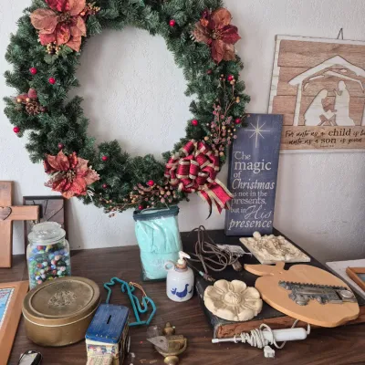 Sale Photo Thumbnail #21: Collection of holiday decor and household items, including a large faux-evergreen Christmas wreath decorated with poinsettias, wooden religious wall art, glass marble jar, and vintage tin bank.