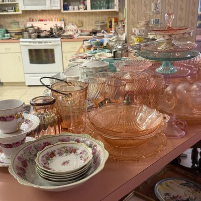 Collection of vintage pink depression glass stemware, cake stands, and porcelain tea cups
