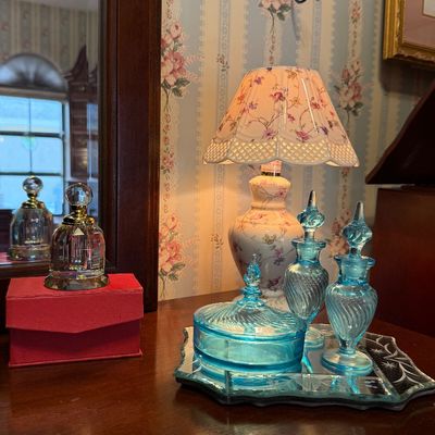 Vintage vanity arrangement featuring a set of blue swirl glass perfume bottles and trinket dish on a mirrored tray, a floral ceramic mini...