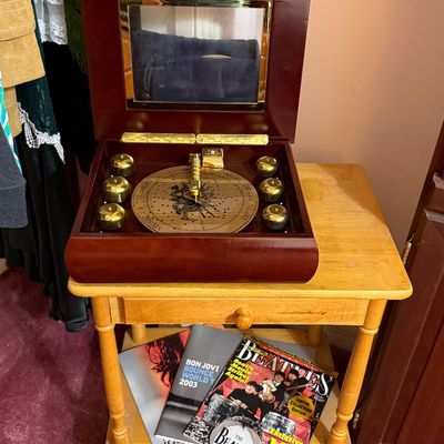 Polished wooden disc music box displayed open on a two-tier wooden end table alongside music tour programs and magazines.