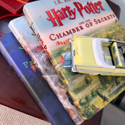 Sale Photo Thumbnail #269: Stack of illustrated Harry Potter hardcover books by J.K. Rowling, topped with a yellow die-cast model 1957 convertible car.