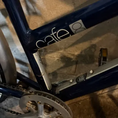 Sale Photo Thumbnail #227: Close-up detail of a dark blue Cafe 8 bicycle frame showing the chain ring, crankset, and brand lettering.