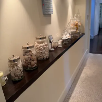 Collection of decorative glass jars filled with seashells and bath items arranged on a built-in hallway shelf.