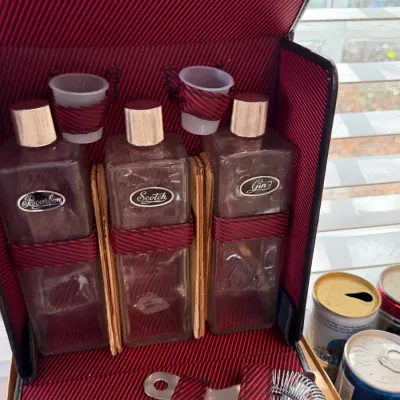 Sale Photo Thumbnail #157: Vintage portable travel bar set featuring three glass liquor decanters labeled Bourbon, Scotch, and Gin, along with shot glasses and bar tools in a red patterned carrying case.
