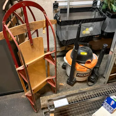 Sale Photo Thumbnail #218: Vintage wood and red metal flexible flyer snow sled leaning against a basement wall alongside a Ridgid wet/dry shop vacuum.