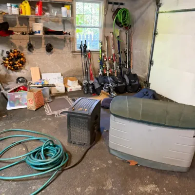 Sale Photo Thumbnail #214: Assorted garage and outdoor items including a plastic deck storage box, hose reel, garden hose, ski equipment, and wall-mounted shelving.