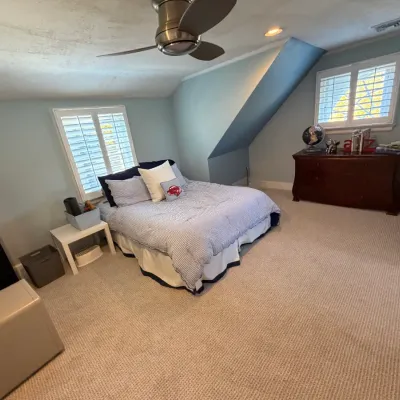 Spacious bedroom set featuring a queen-size bed frame with blue and white striped bedding, accompanied by a dark wood dresser, a white...