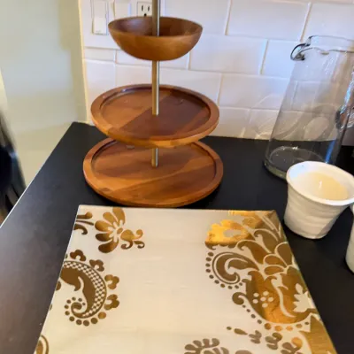 Sale Photo Thumbnail #184: Selection of kitchen servingware, including a three-tiered wooden tray, a square gold-patterned glass plate, a glass pitcher, and small ceramic containers.