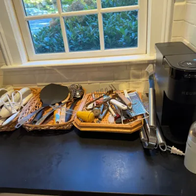Sale Photo Thumbnail #180: Collection of small kitchen appliances and utensils, including a Keurig single-serve coffee maker, coffee grinder, and woven baskets filled with assorted cooking tools.