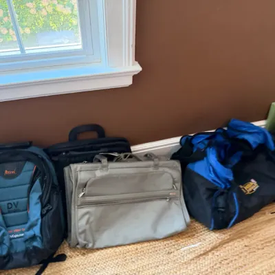 Sale Photo Thumbnail #101: Collection of modern luggage and bags lined up on the floor, including a Petrol camera backpack, a Tumi travel bag, and a blue sports duffel.