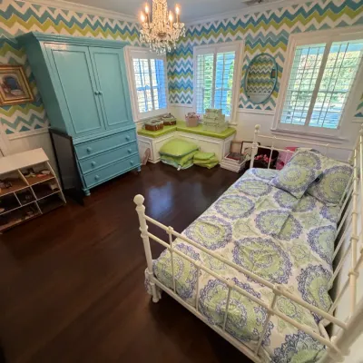 White metal daybed frame with a matching blue and green patterned bedding set inside a bedroom featuring a bright turquoise armoire.