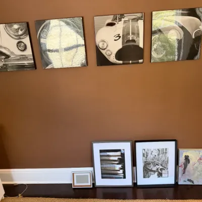 Sale Photo Thumbnail #107: Set of four square black-and-white classic automobile prints mounted on a wall, shown above several framed picture frames and canvas art leaning on the floor.