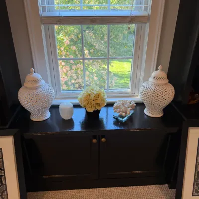 Pair of white reticulated lattice temple jars flanking decorative items on a dark-painted window bench cabinet.