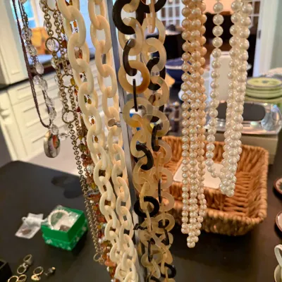 Sale Photo Thumbnail #205: Collection of vintage fashion necklaces displayed on a T-bar stand, including faux pearl strands, Lucite chain links, and beaded pieces.