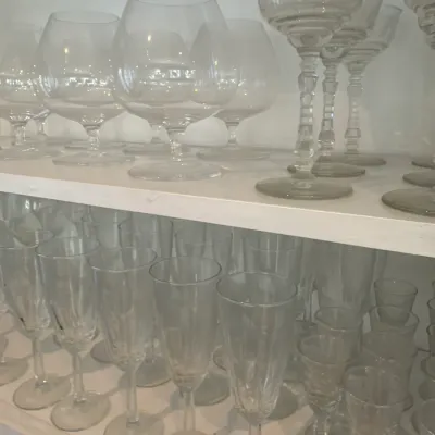 Sale Photo Thumbnail #162: Collection of clear crystal stemware including brandy snifters, cocktail glasses, and champagne flutes arranged on white shelves.