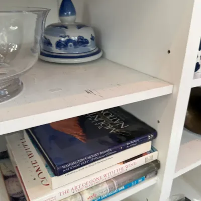 Sale Photo Thumbnail #145: White wooden bookshelf filled with coffee table books, clear glassware, and a blue and white Asian porcelain covered jar.