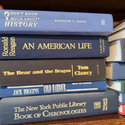 Sale Photo Thumbnail #250: Stack of hardcover books including Ronald Reagan's An American Life, Tom Clancy's The Bear and the Dragon, and reference volumes, displayed on a wooden shelf.