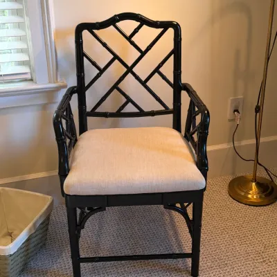 Hollywood Regency style black faux bamboo armchair featuring a geometric fretwork backrest and a light beige upholstered seat cushion.