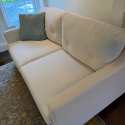 Sale Photo Thumbnail #131: Contemporary off-white upholstered sofa featuring button-tufted back cushions and straight track arms, accompanied by a single blue-grey accent pillow.