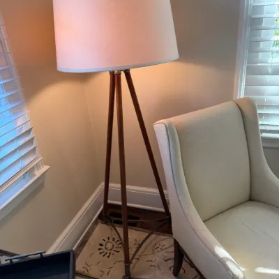 Sale Photo Thumbnail #166: Modern tripod floor lamp with wooden legs and a white drum shade, positioned beside an upholstered cream accent chair.