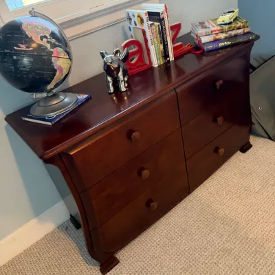 Dark cherry wood six-drawer dresser with curved side profile and matching wooden knobs, topped with decor including a desk globe, books,...