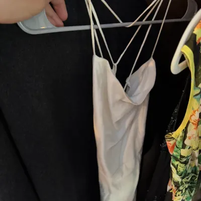 White satin slip dress with a cowl neckline and multi-strap back design, displayed on a plastic hanger.