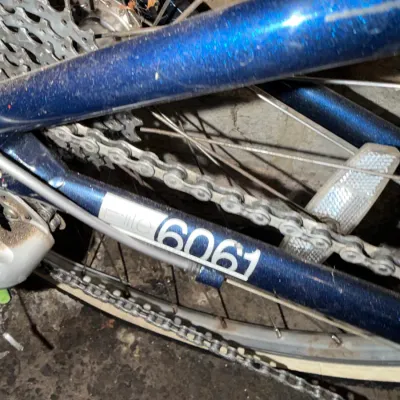 Sale Photo Thumbnail #228: Close-up of a blue metallic bicycle frame featuring a 6061 aluminum tubing decal and rear wheel assembly.
