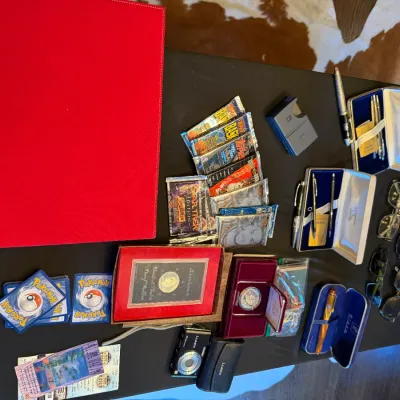 Sale Photo Thumbnail #172: Collection of collectibles including sealed sports and trading card packs, Pokémon cards, boxed pen sets, commemorative coins, sunglasses, cufflinks, and a Panasonic Lumix digital camera.
