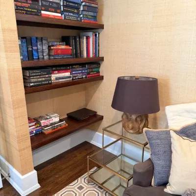 Cozy reading nook featuring built-in wooden bookshelves filled with books, a brass-framed glass tiered end table, and a contemporary...