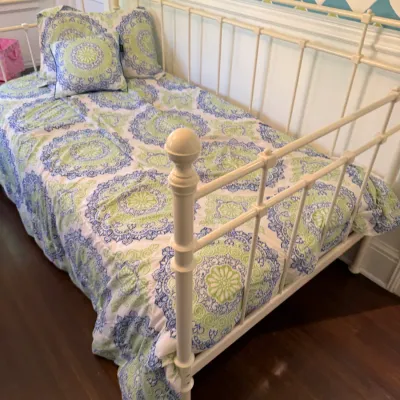 Off-white metal spindle daybed frame with ball finials, dressed in a blue and green mandala patterned comforter with matching pillows.