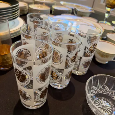Sale Photo Thumbnail #186: Set of vintage highball glasses featuring white frosted and gold printed geometric motifs, displayed alongside china plates and cut crystal glassware.
