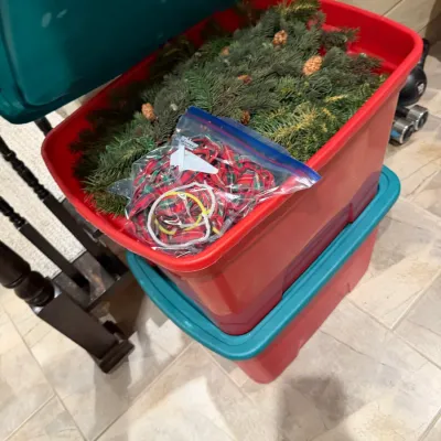Sale Photo Thumbnail #261: Stacked plastic storage totes filled with holiday decorations, including faux evergreen garland and plaid ribbon.