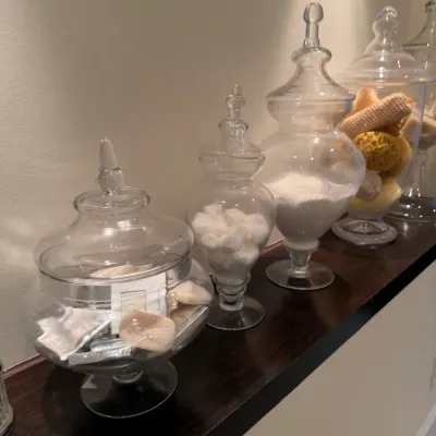 Collection of clear glass apothecary jars in various shapes and sizes, filled with bathroom accessories and toiletries.