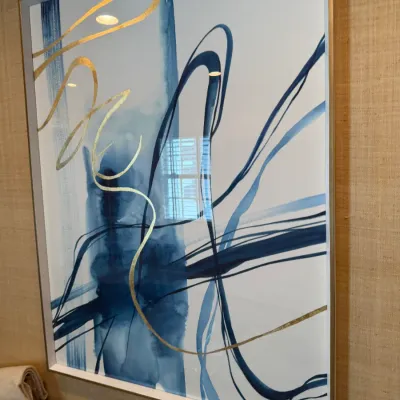 Sale Photo Thumbnail #211: Large contemporary abstract wall art featuring blue watercolor splashes and metallic gold calligraphic lines, framed under glass in a thin brass-toned frame.