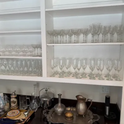 Sale Photo Thumbnail #159: Collection of crystal stemware, champagne flutes, beer glasses, and silver-plated barware displayed on built-in shelving.