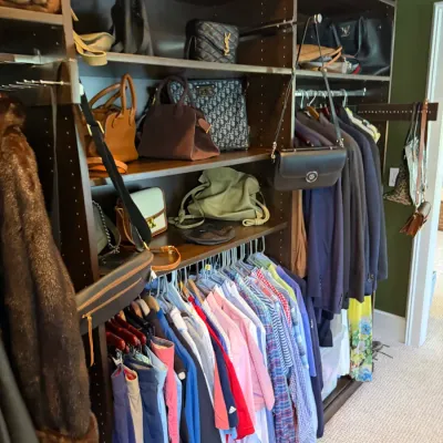 Dark wood built-in walk-in closet system filled with designer handbags, coats, and men's dress shirts.