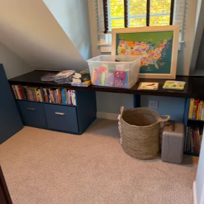 Built-in long desk with blue storage bases holding various books, a clear storage bin, a framed US map, and a woven floor basket.
