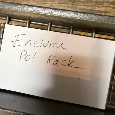 Sale Photo Thumbnail #245: Handwritten paper label for an Enclume pot rack resting on a metal grate.