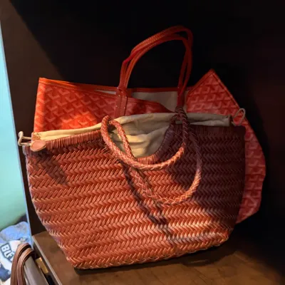 Two designer style handbags resting on a shelf, including a woven brown leather tote bag with braided handles and an orange chevron...