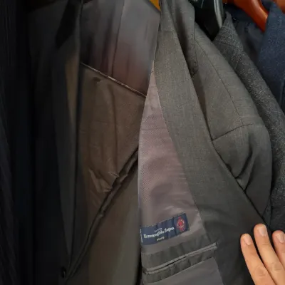 Sale Photo Thumbnail #240: Men's charcoal gray suit jacket made with Ermenegildo Zegna Shang fabric, displayed on a wooden Brooks Brothers hanger inside a closet.