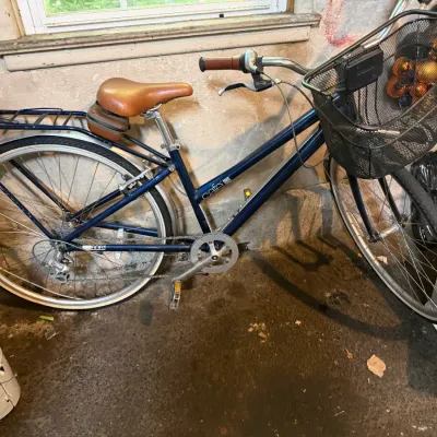 Sale Photo Thumbnail #226: Blue Cafe 6061 step-through commuter bicycle equipped with a front wire basket, rear cargo rack, and brown leatherette seat.