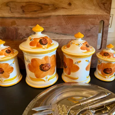 Sale Photo Thumbnail #182: Vintage four-piece ceramic canister set featuring hand-painted orange floral designs and yellow finial lids, arranged in front of a wooden cutting board.