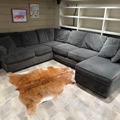 Sale Photo Thumbnail #260: Large dark gray sectional sofa paired with a natural brindle cowhide rug in a finished basement room.