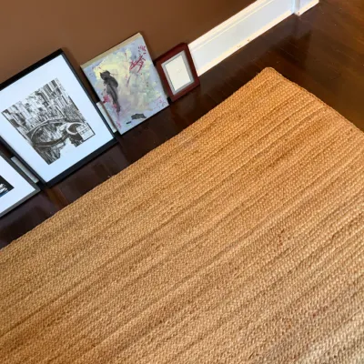 Sale Photo Thumbnail #108: Natural woven jute area rug paired with a collection of framed wall art leaning against a baseboard.