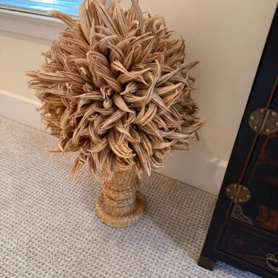Dried okra pod sphere topiary displayed on a woven urn base, featuring a distinctive organic texture.