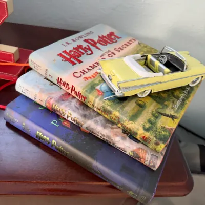 Sale Photo Thumbnail #268: Stack of three Harry Potter illustrated edition hardcover books with a die-cast yellow convertible toy car displayed on top.