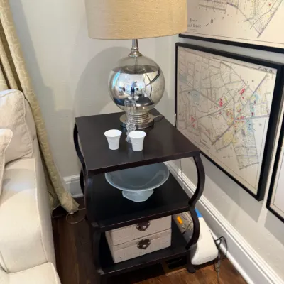 Sale Photo Thumbnail #112: Modern dark wood three-tier end table featuring a spherical silver glass table lamp with a linen shade, small ceramic cups, a serving bowl, and storage boxes.