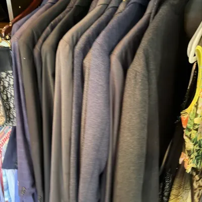Collection of men's suit jackets and blazers in dark tones hanging in a closet.