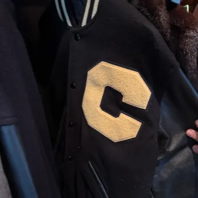 Vintage black wool varsity jacket featuring leather sleeves and a large yellow felt 'C' letterman patch, hanging in a closet.